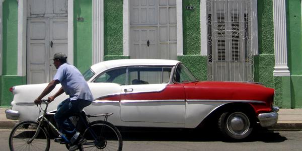 A man cycles through the streets of Havana, passing an old-fashioned American car