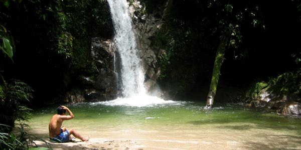 Boy sitting by waterfall at Cloud Forest, Ecuador.