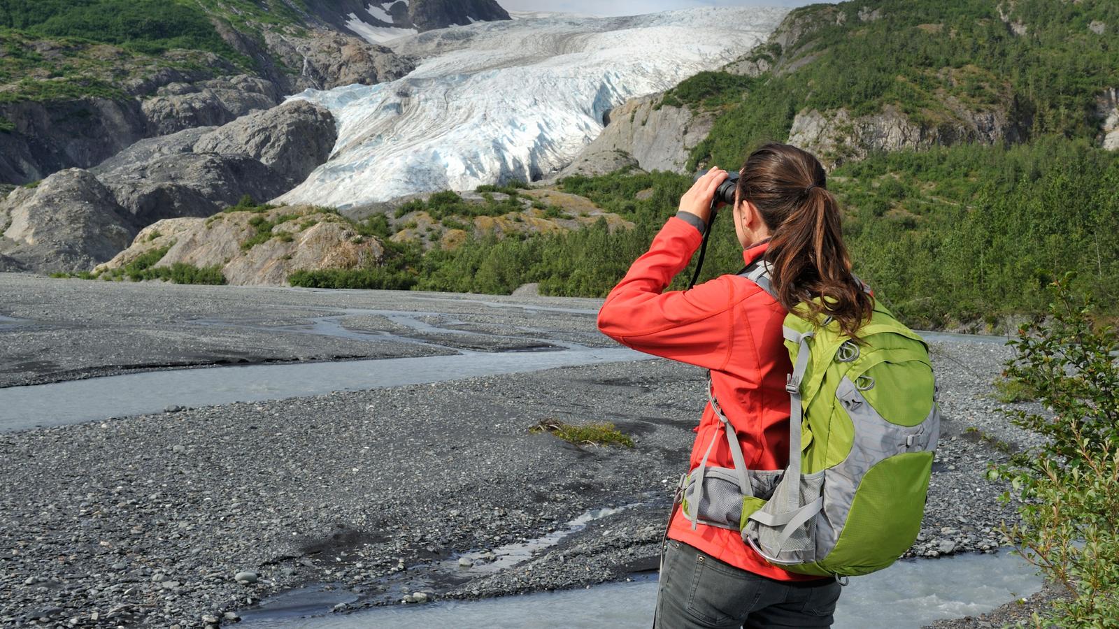 A female trekker zooming in on scenery with her binoculars in Alaska
