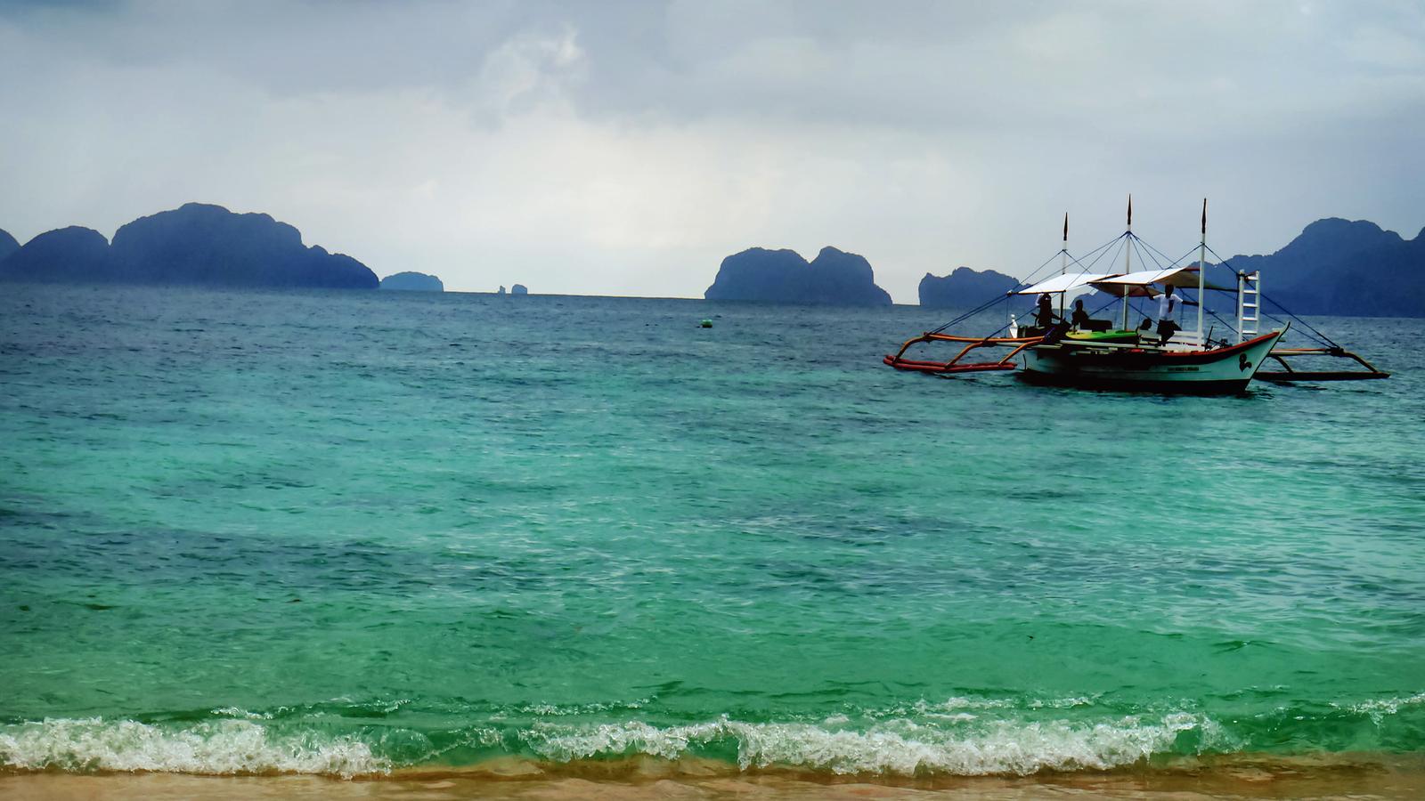 A boat floats near the turquoise coast of El Nido island in the Philippines