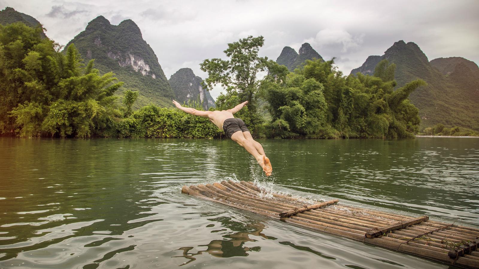 Traveller jumping off a bamboo raft into the river in Yangshuo, China