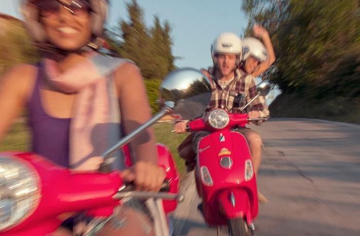 Three happy tourists on red scooters in Tuscany, Italy