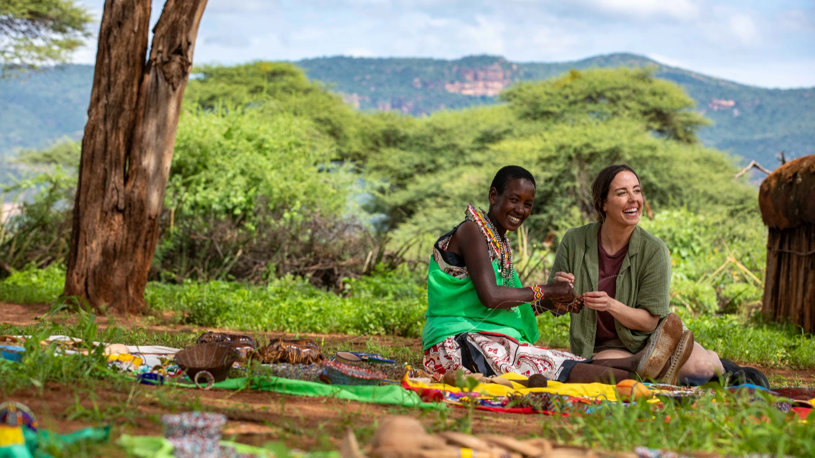 A G Adventures traveller sitting with a local Maasai woman, sharing a craft activity outdoors in Kenya